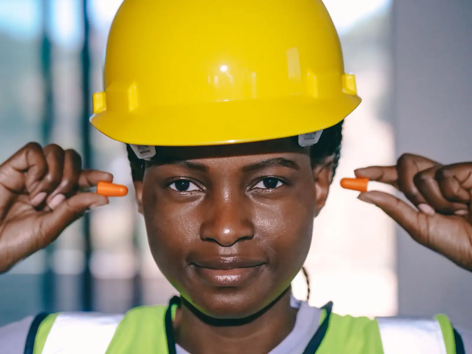 Worker in a hard hat and safety vest holding foam earplugs